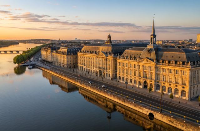 Vue aérienne des quais bordelais et du miroir d'eau à heure dorée, façade calcaire 18e siècle de la Place de la Bourse reflétée dans l'eau