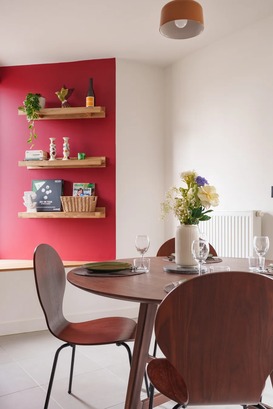 Coin repas de L'Esplanade avec table ronde et mur framboise
