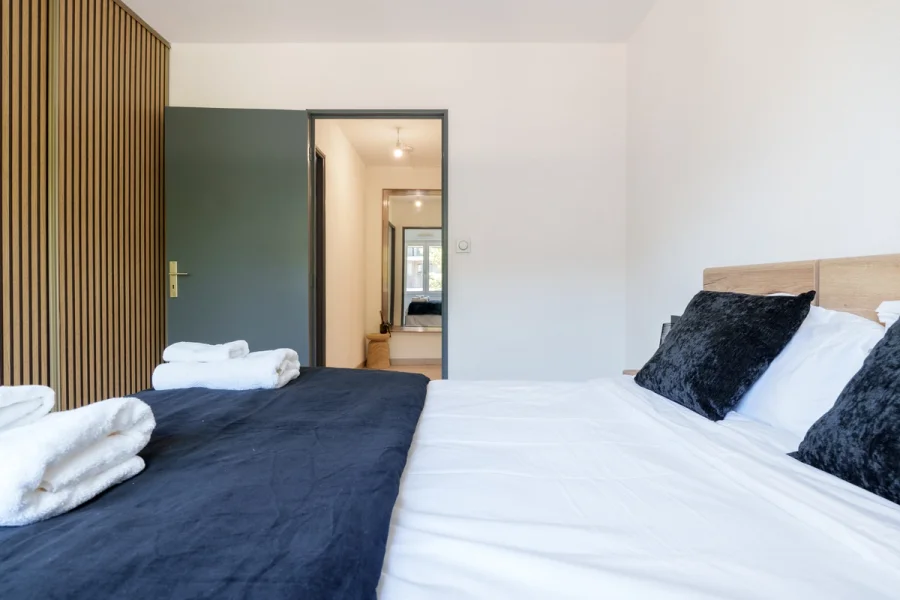 Chambre avec serviettes pliées sur le lit, ouverte sur l'entrée