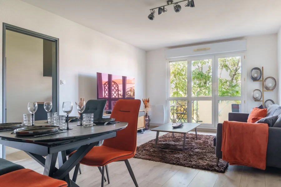 Coin repas du séjour dressé pour quatre, ouvert sur la terrasse