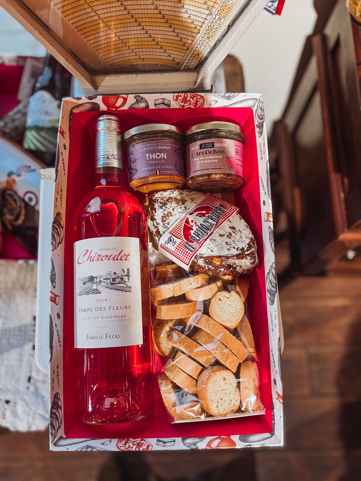 Coffret cadeau rouge avec une bouteille de rosé, des terrines et des biscuits