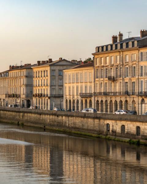 Quais des Chartrons vus depuis la Garonne, façades 18e siècle reflétées dans l'eau calme, Pont de Pierre en arrière-plan, lumière dorée