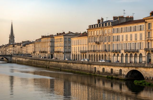 Quais des Chartrons vus depuis la Garonne, façades 18e siècle reflétées dans l'eau calme, Pont de Pierre en arrière-plan, lumière dorée