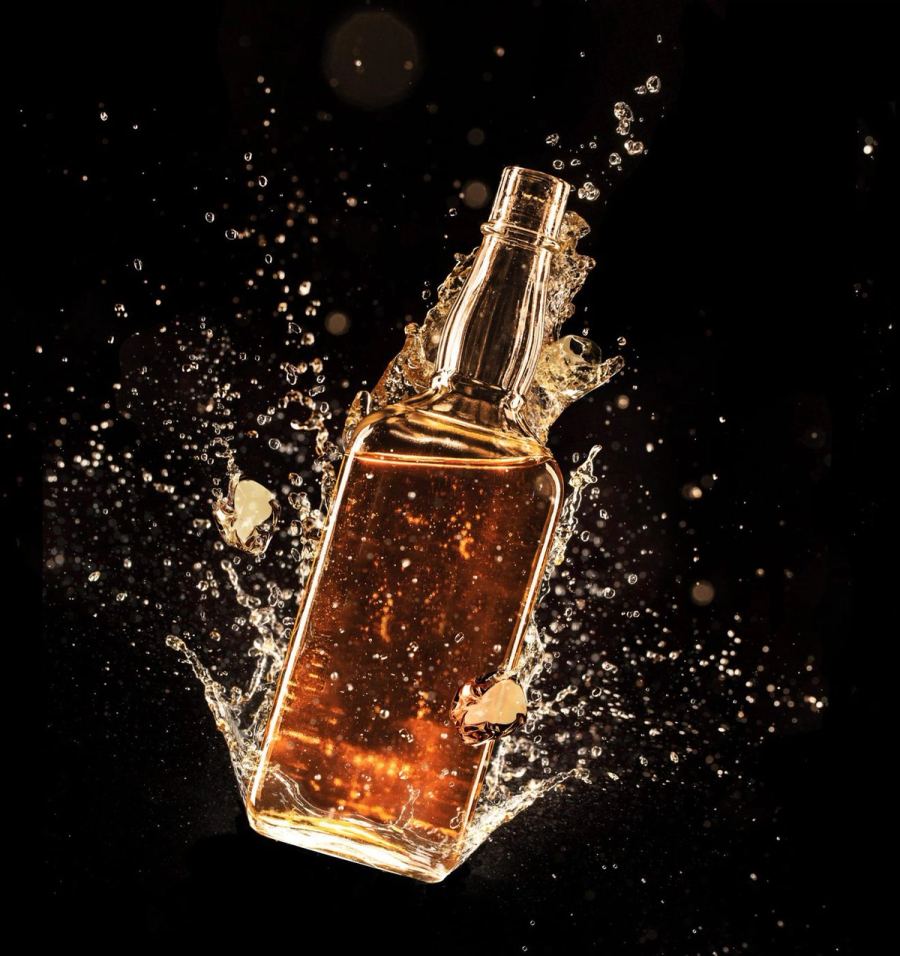 Gold coated bottle photographed in a liquid splash on black