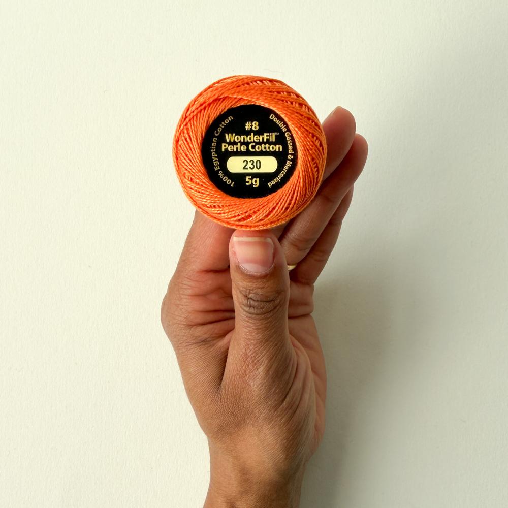 Ei hand held ei orange nøste med perlegarn framfor ein kvit bakgrunn