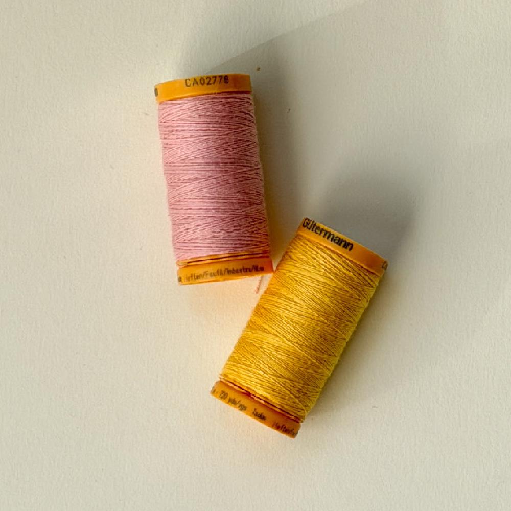 To sneller med sytråd i rosa og gul på lyst underlag