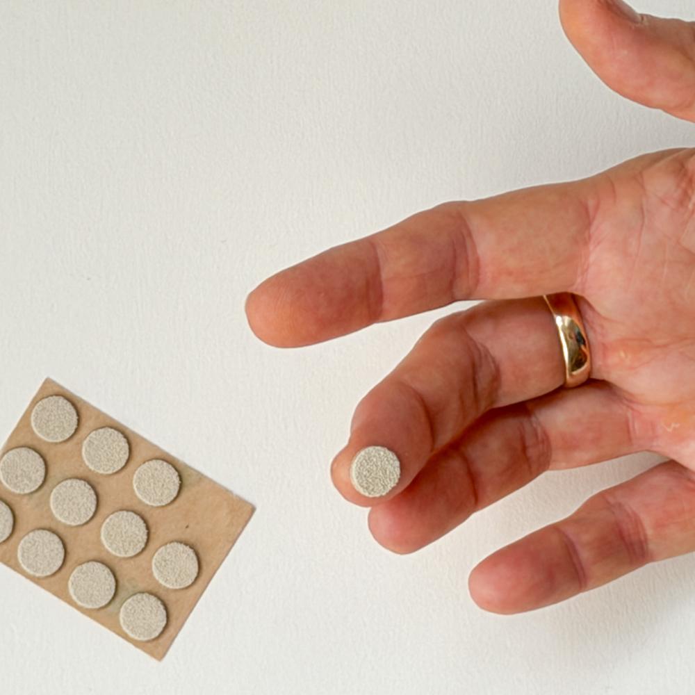 Ei hand held ei lita rund skive av lêr ved sida av eit ark med sjølvklistrande fingervern