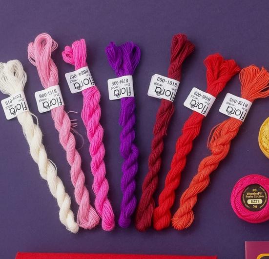 Handbrodert julekula i raud ull med rosa blomster og lilla blad heng på ei granbarjonge