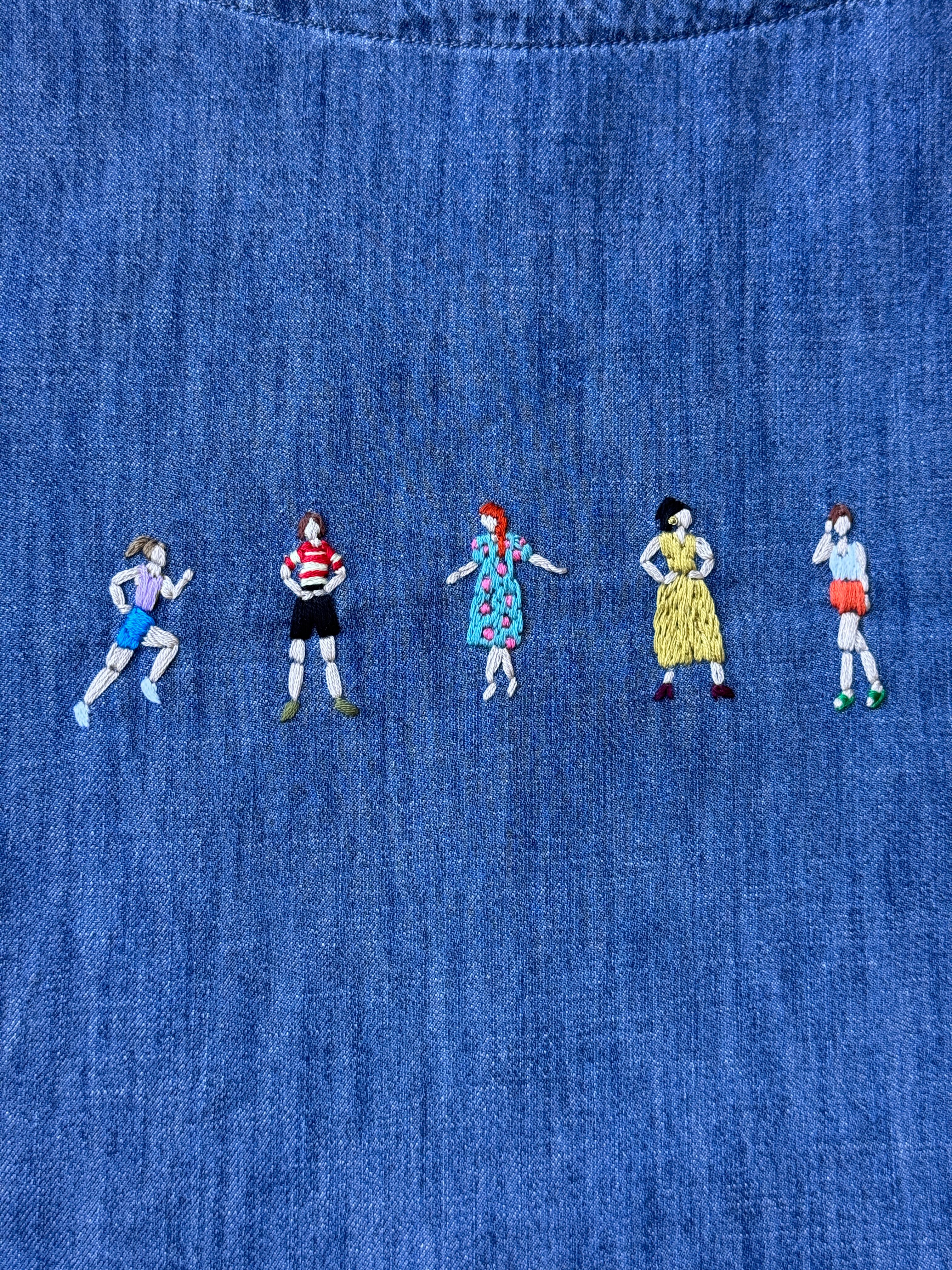Broderi av fem små menneskefigurar med ulike klede på blått stoff