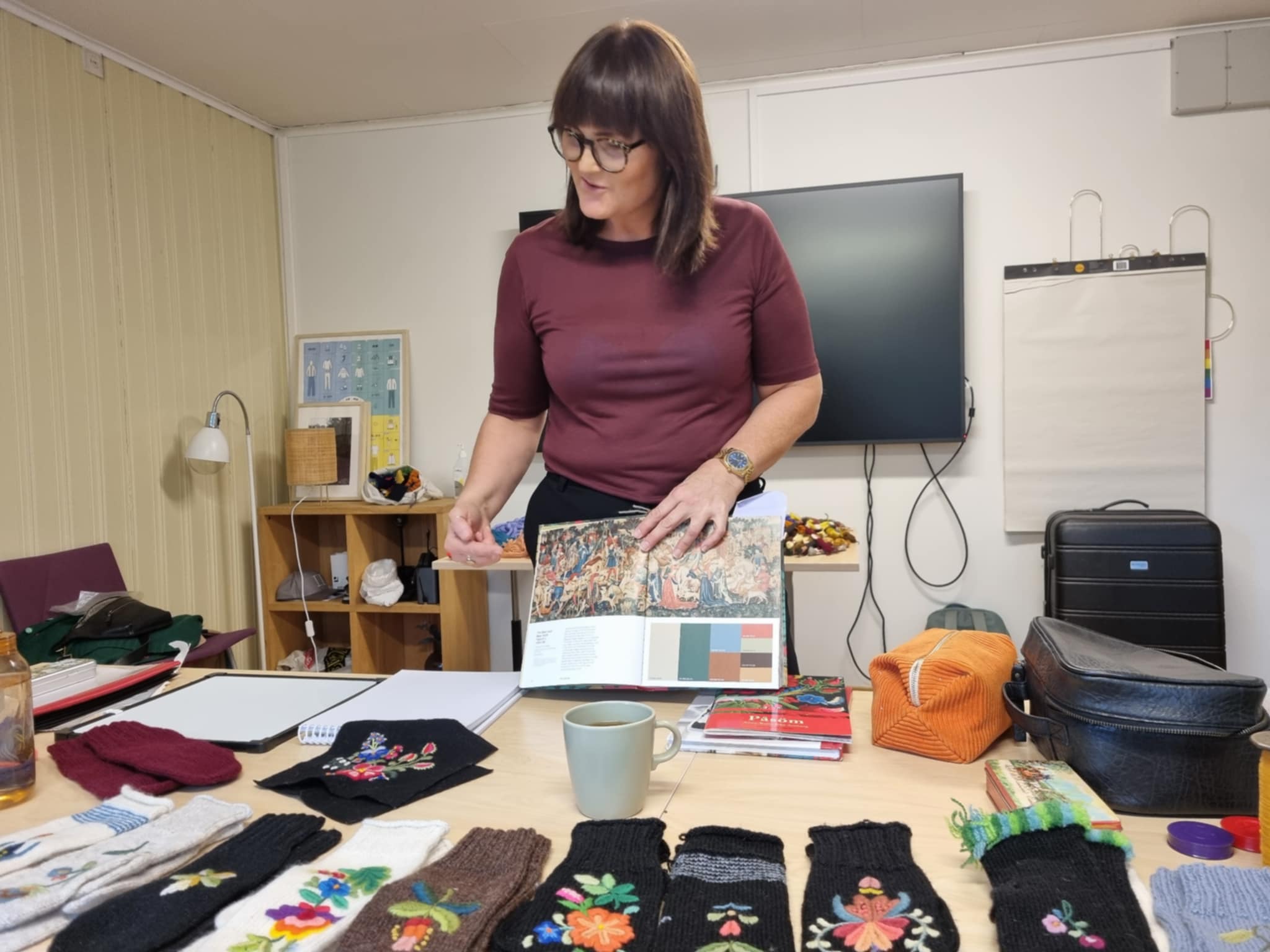 Kvinne ved arbeidsbordet sitt med broderte tekstilar