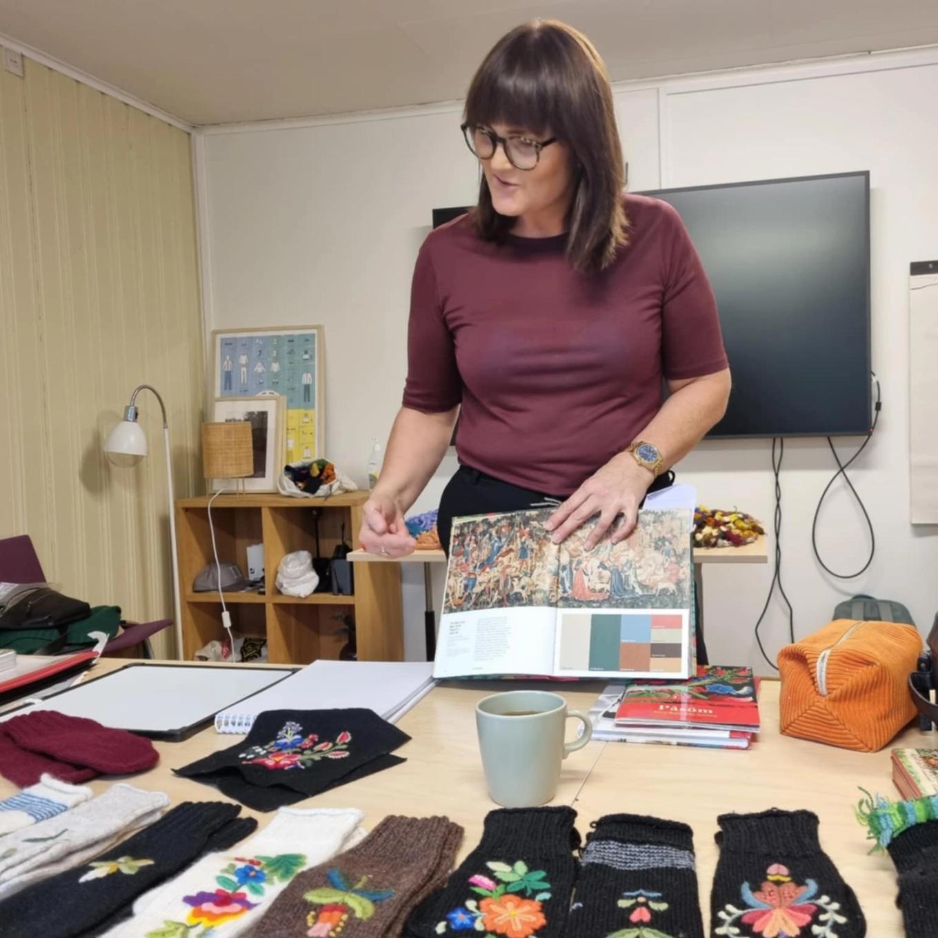 Kvinne ved arbeidsbordet sitt med broderte tekstilar