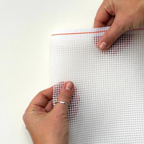 Hender held opp ei kvit stramei med 2,6 trådar per centimeter og ei markering i raudt på kanten