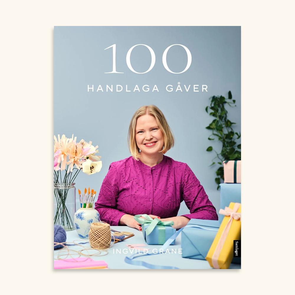 Bokomslag for 100 handlaga gåver av Ingvild Grane med smilande kvinne omringa av heimelaga gåver og hobbymateriell