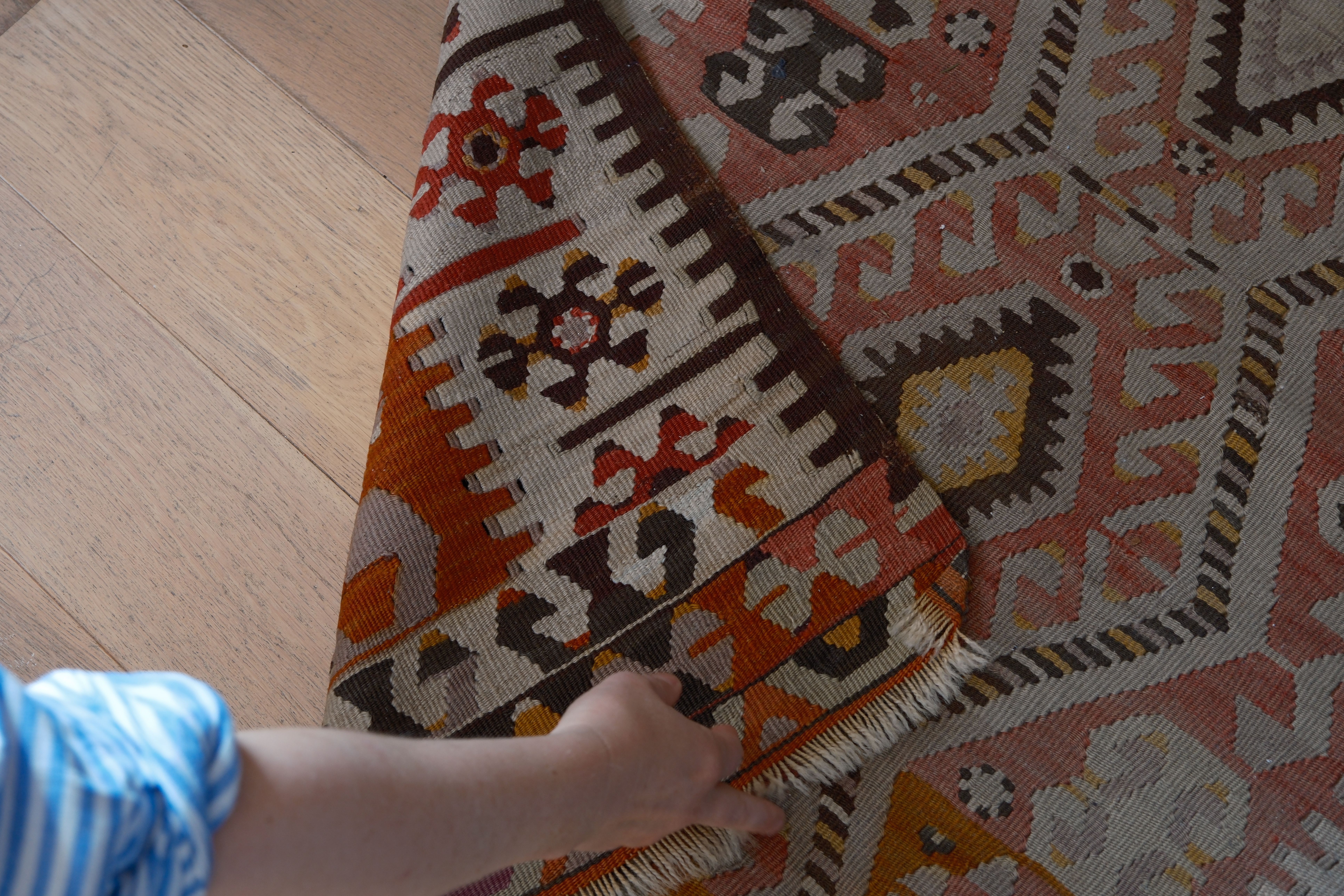 Hender som brettar ei vevd kilim-matte i ull med geometriske mønster.