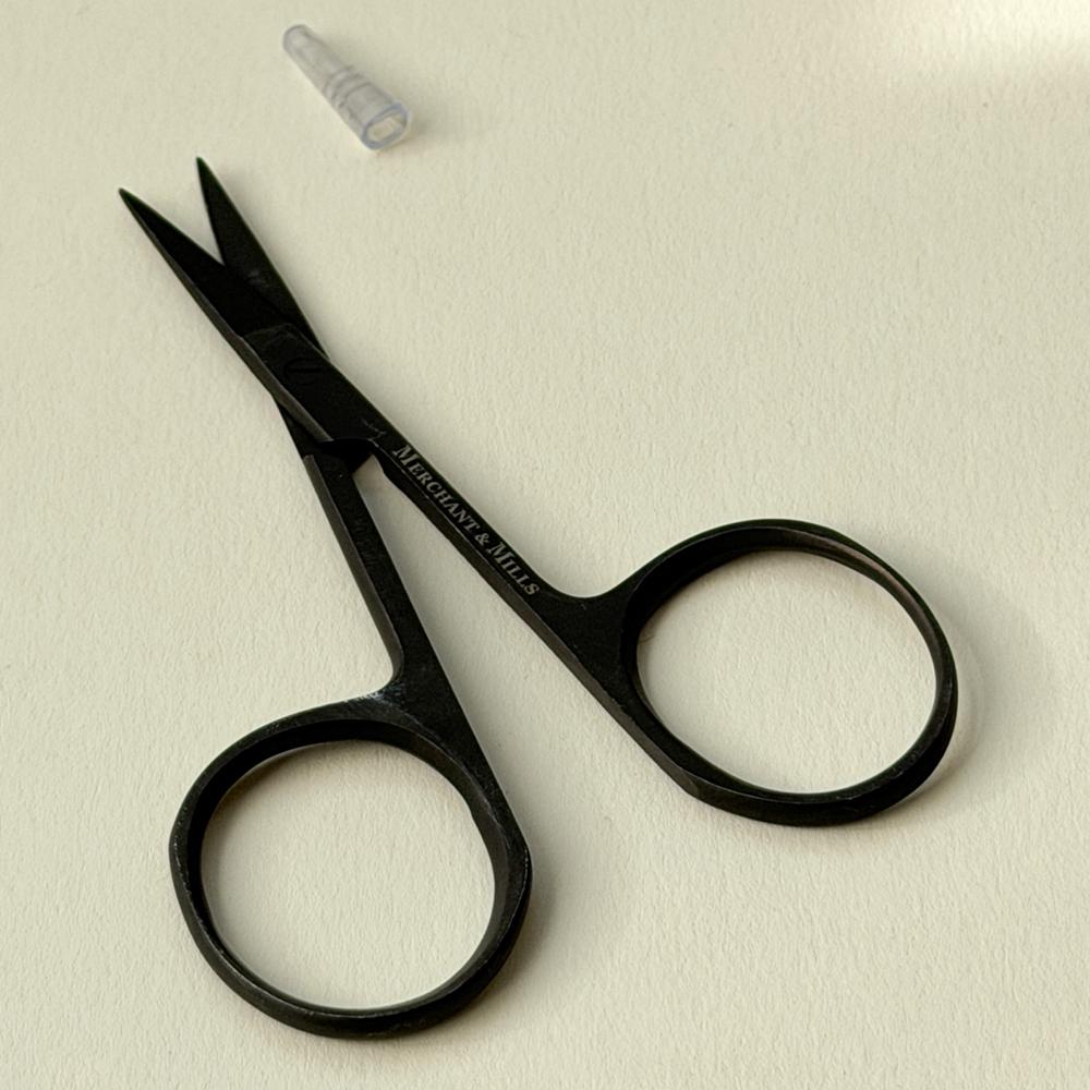 Svart broderisaks ligg på lyst underlag med ein liten gjennomsiktig beskyttathet for spissen ved sida av