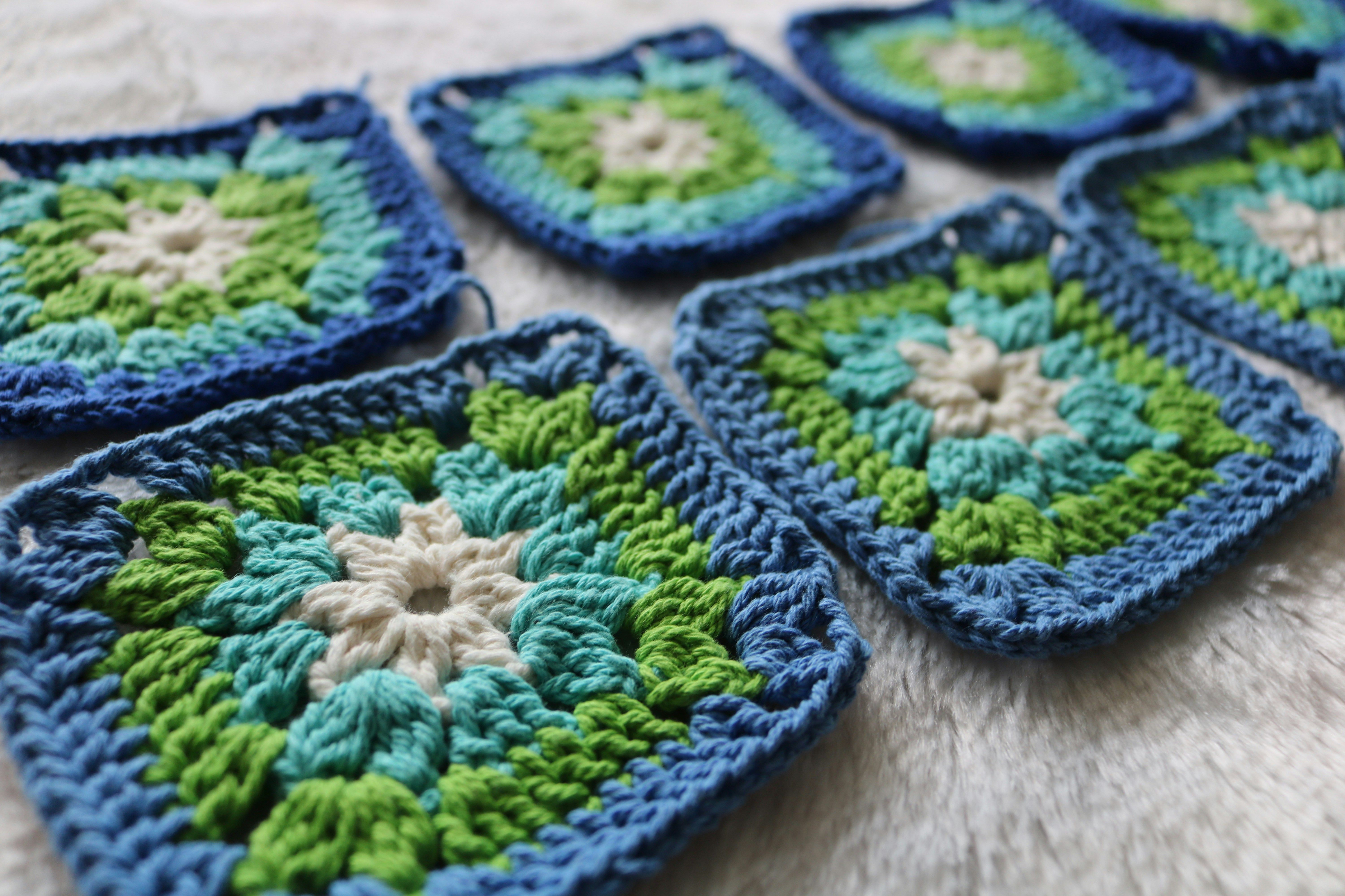 Hekla granny squares i blått, grønt og kremfarga, lagde ut på ei lys, lodden overflate
