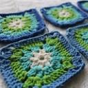 Hekla granny squares i blått, grønt og kremfarga, lagde ut på ei lys, lodden overflate
