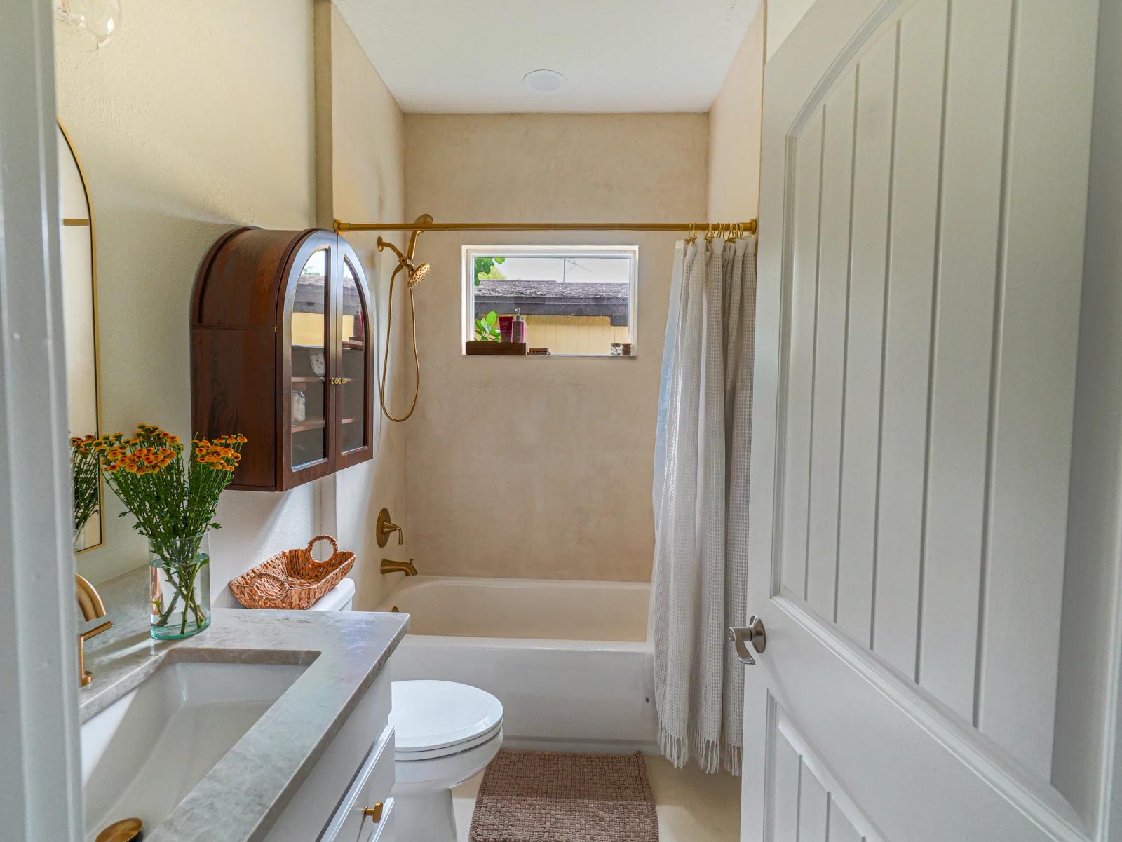 View through the bathroom door: microcement tub surround, vanity and arched wall cabinet