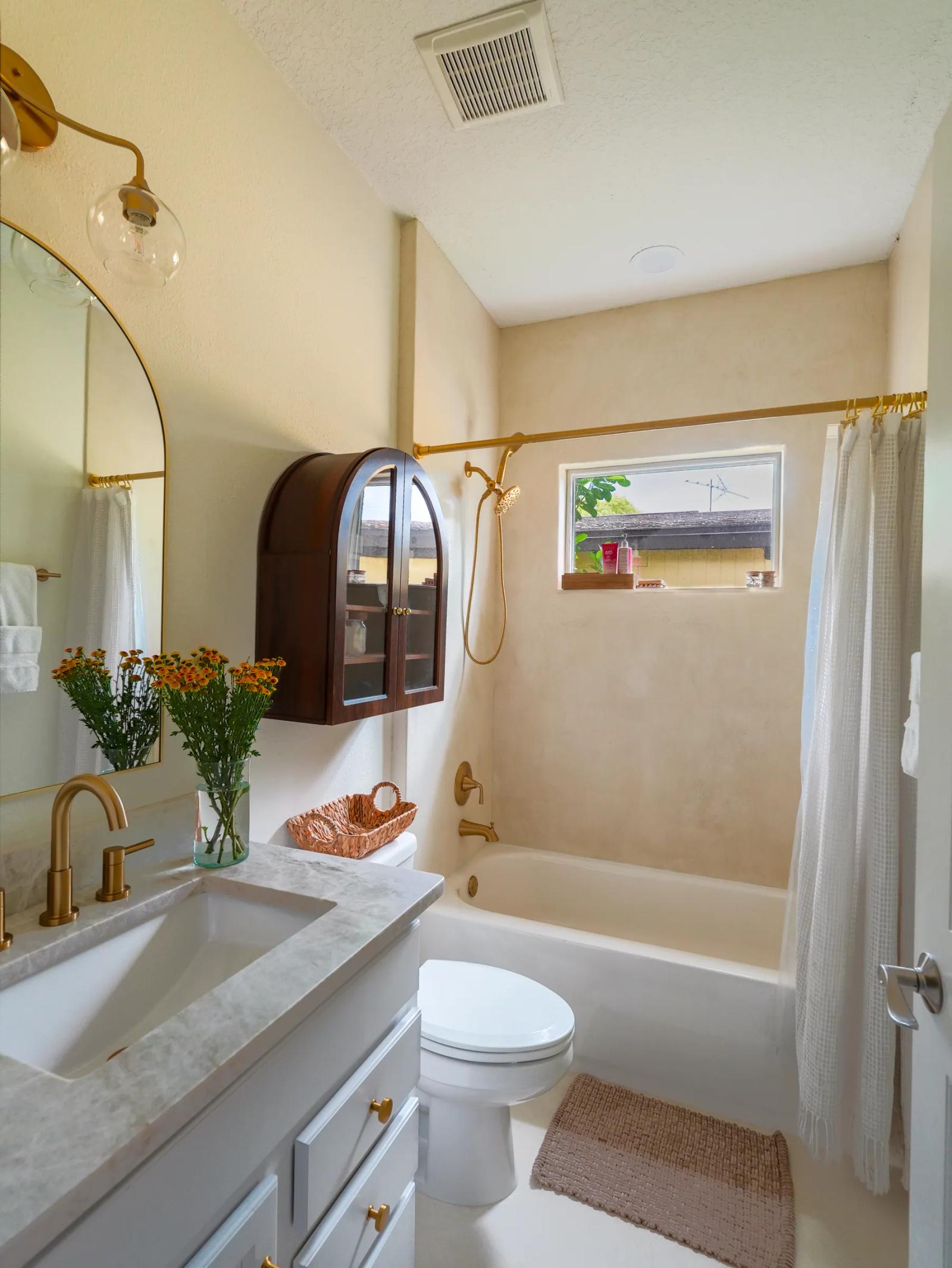 Full view of the bathroom with microcement walls, tub, vanity and brass fixtures