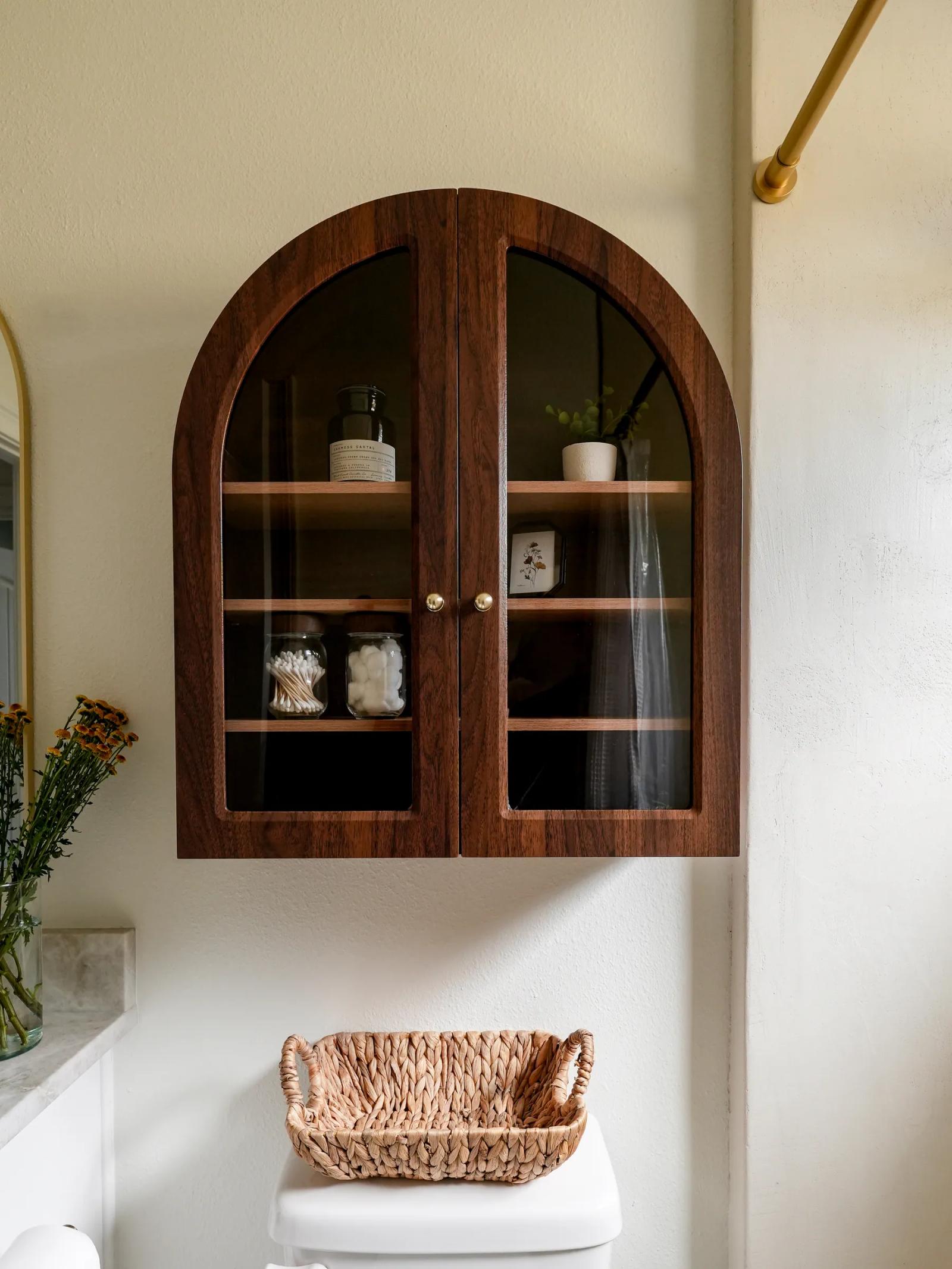 Arched dark-wood glass cabinet mounted above the toilet on a microcement wall