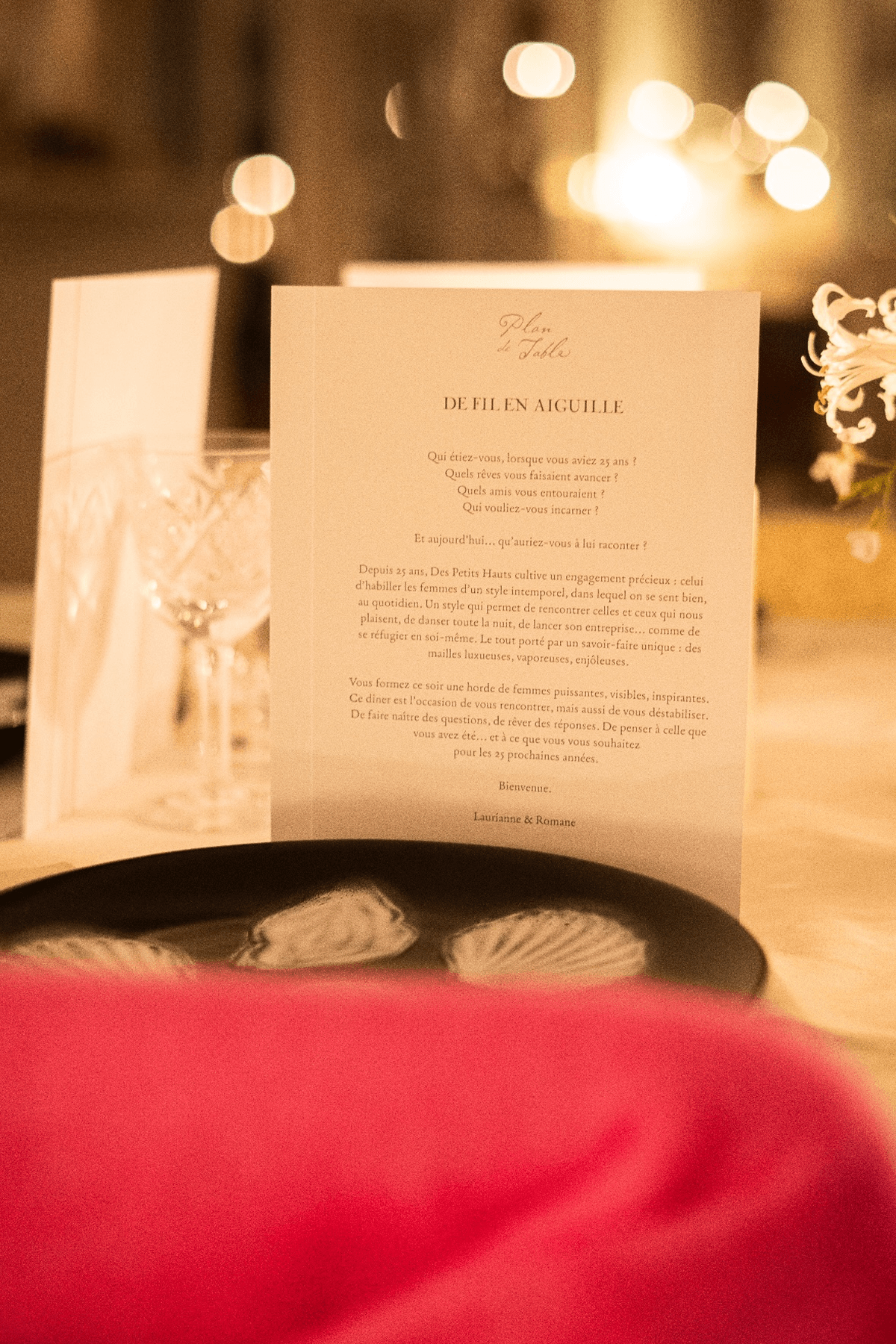 Close-up of a printed dinner program titled "De Fil en Aiguille" in a soft candle lit setting.
