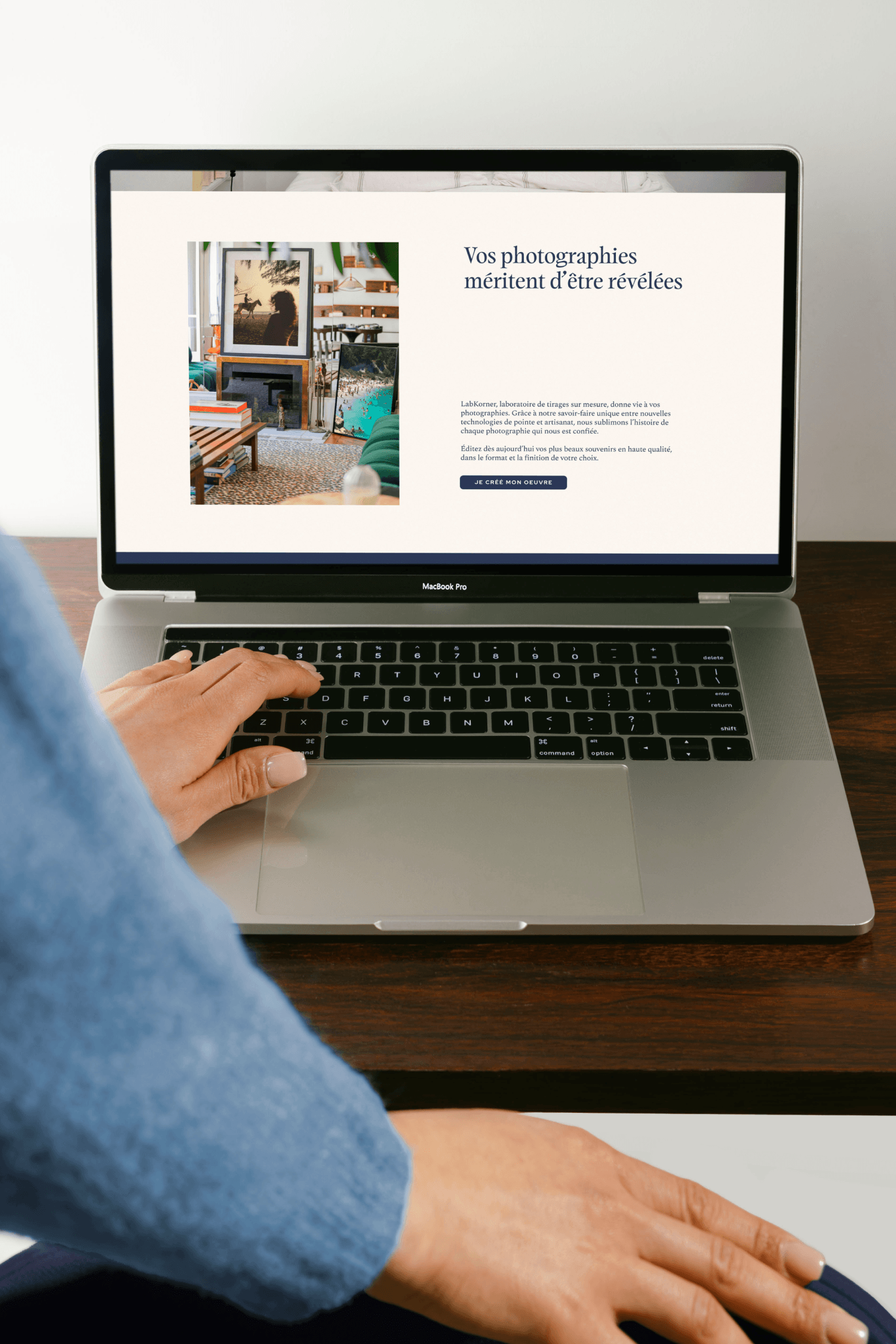 Close-up of hands typing on a laptop displaying the LabKorner website homepage, with the tagline "Vos photographies méritent d'être révélées" and a framed photo graphic.