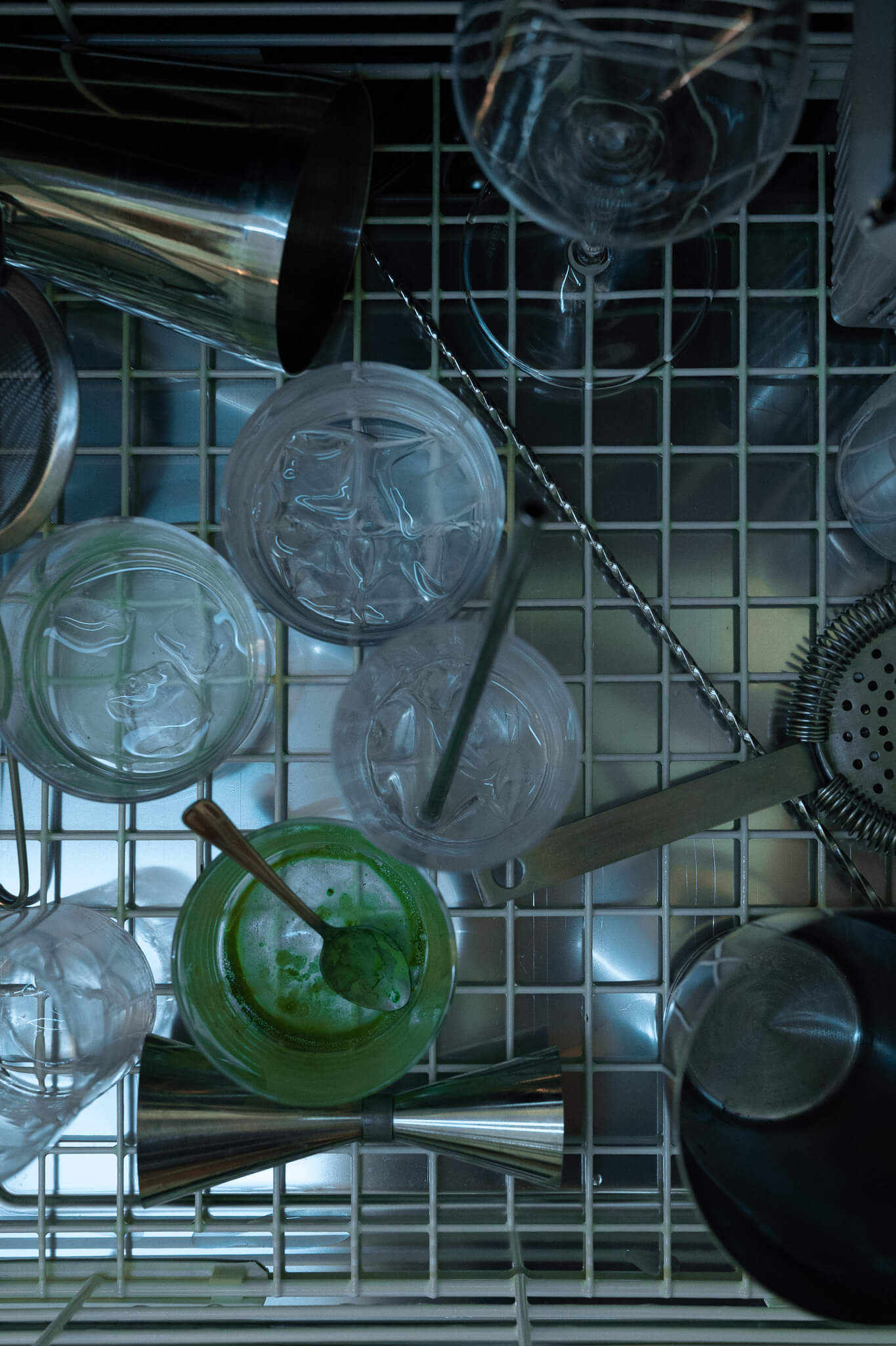 Overhead view of a bar dishwasher with a cocktail shaker, mixing glasses, and a green cocktail.