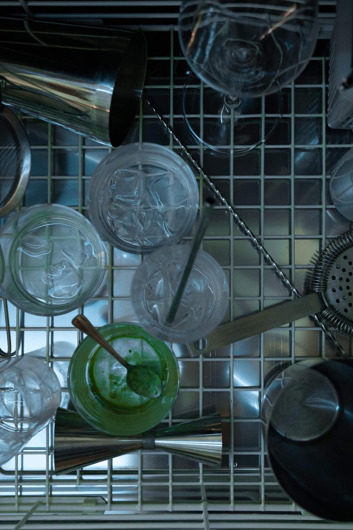 Overhead view of a bar dishwasher with a cocktail shaker, mixing glasses, and a green cocktail.