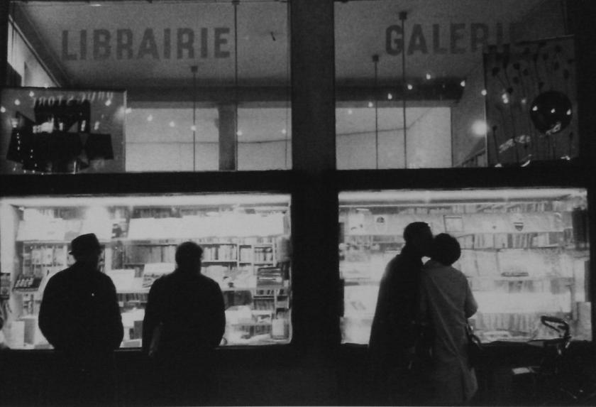 Black and white photograph of La Hune bookshop-gallery's window at night, with silhouettes of passersby