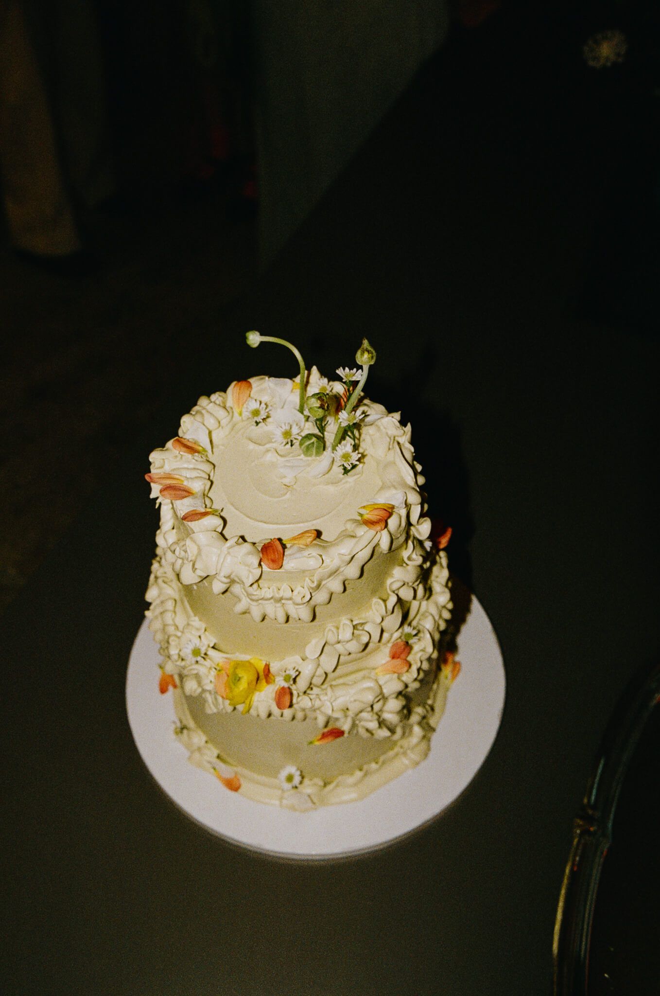 A tiered yellow cake decorated with fresh flowers, photographed in flash.