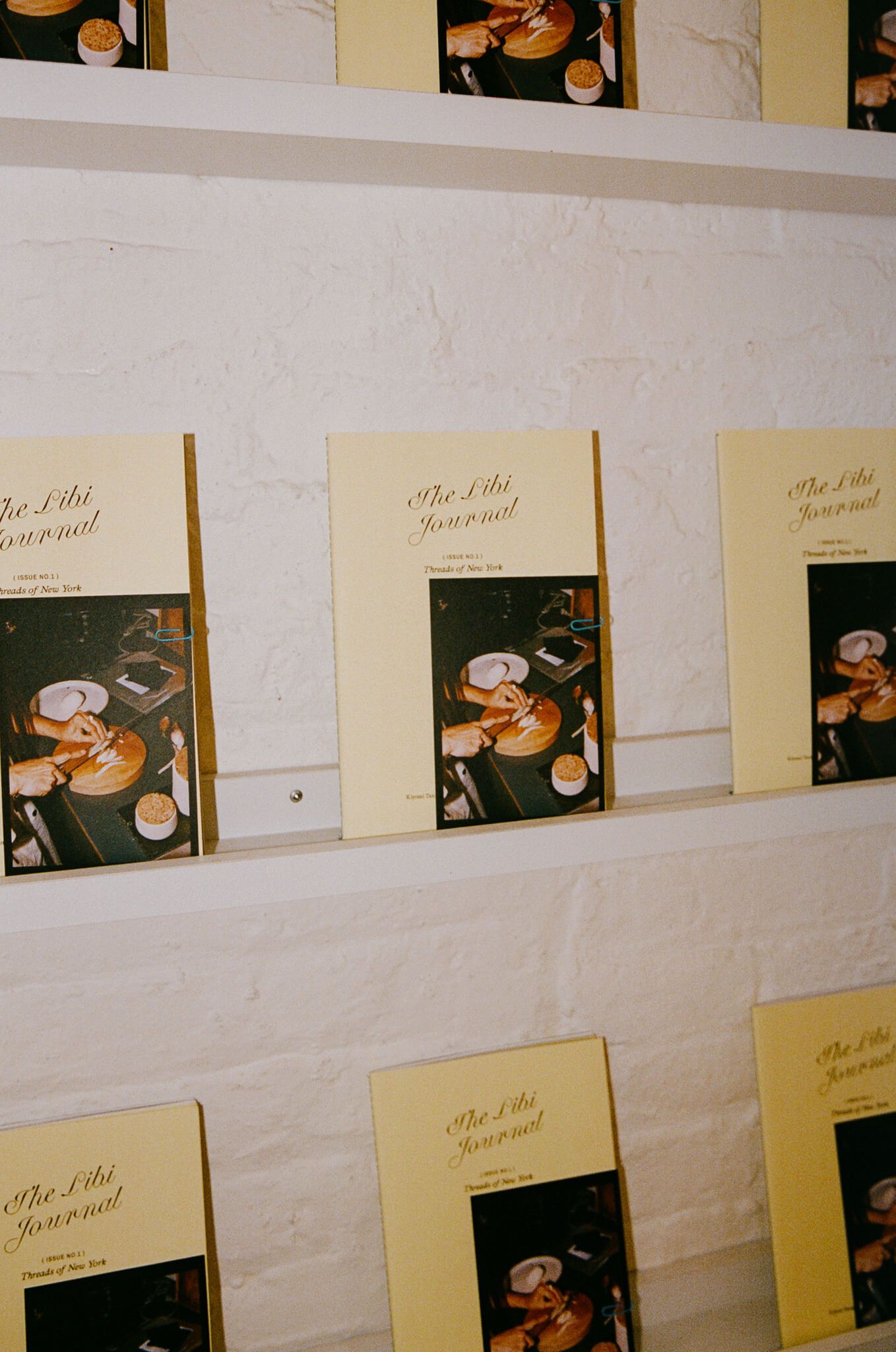 A wall display of journal covers, each paired with a small printed photo, mounted in rows.