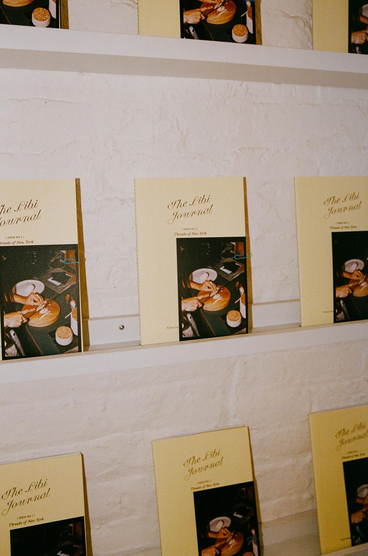 A wall display of journal covers, each paired with a small printed photo, mounted in rows.
