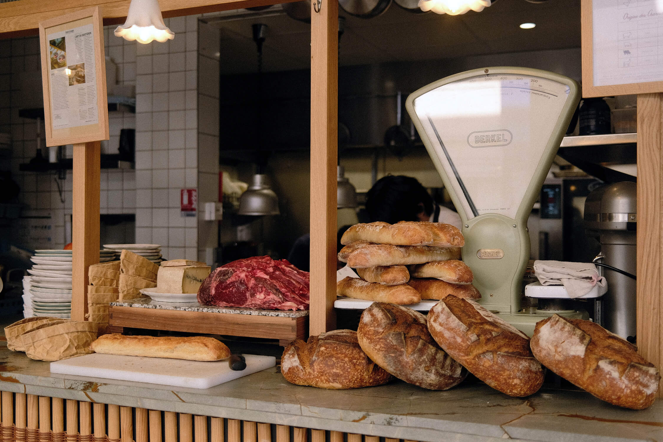 Restaurant counter display inside the bistro, showing fresh bread loaves, cured meats, cheese, and a vintage scale under warm lighting.