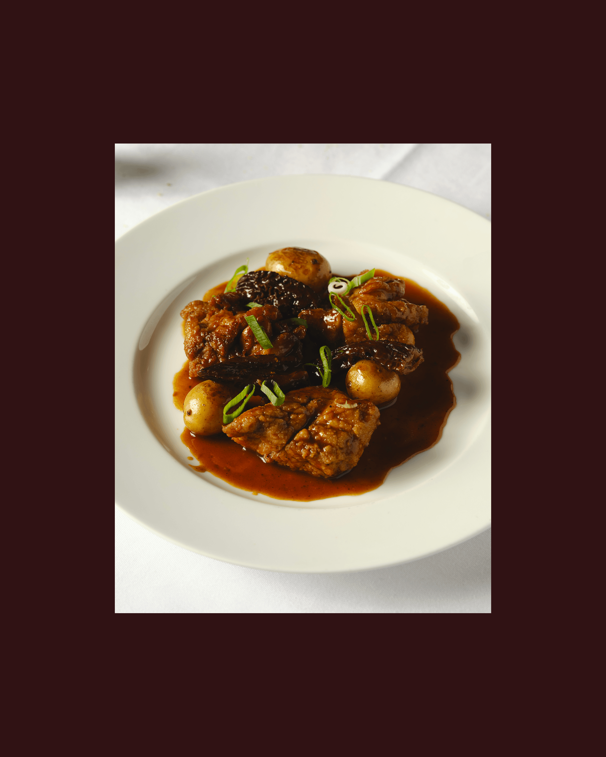 A plated dish of glazed meat and small onions in dark sauce, overlayed on a burgundy background.