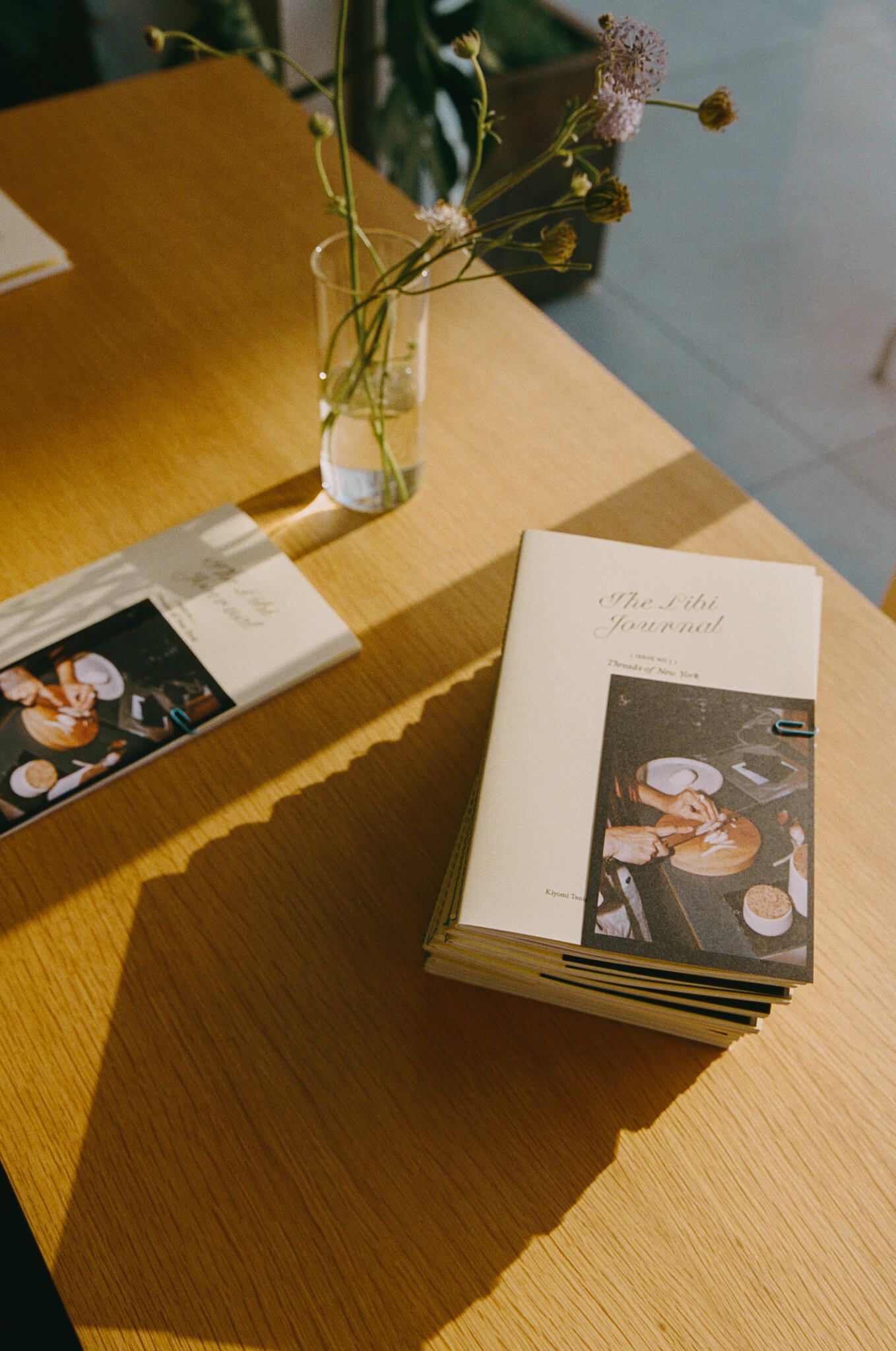Left: a stack of journals on a wooden table beside a small vase of flowers and a photo print.