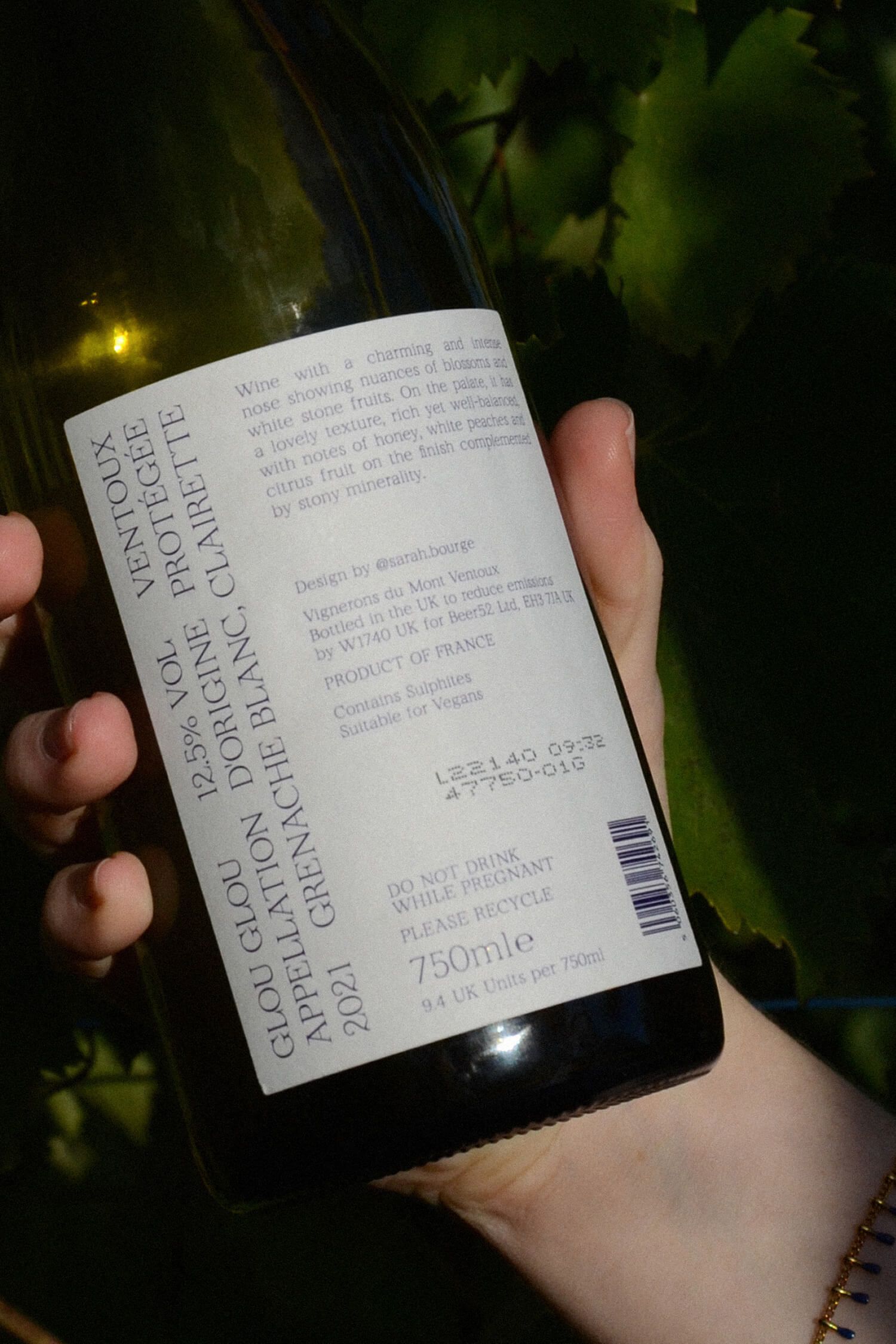 Close-up of the back label held against vine leaves, showing tasting notes and production details in white text on the dark bottle.