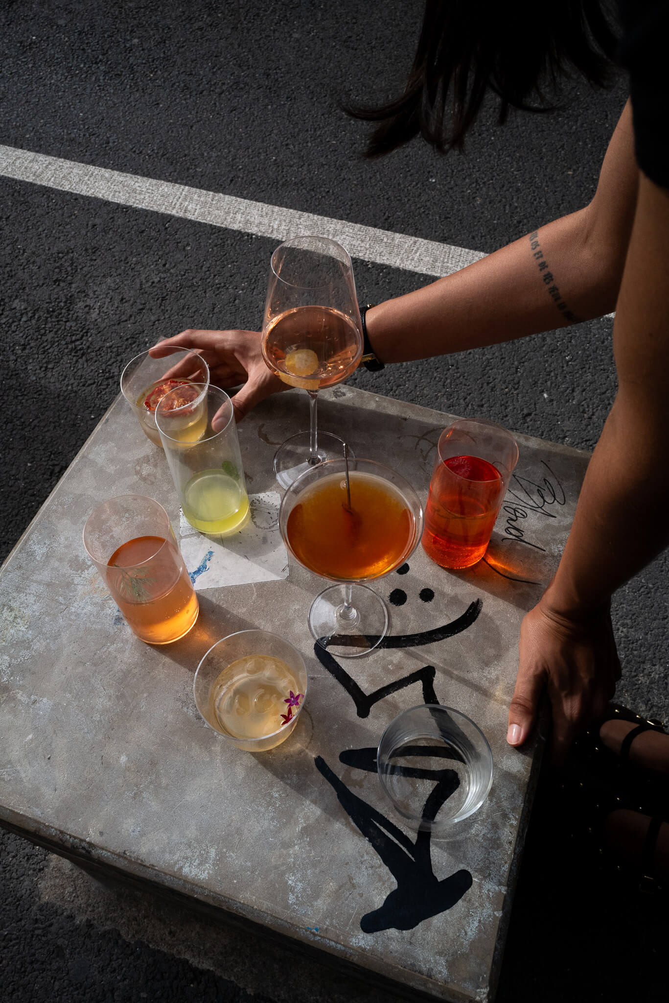 Overhead shot of a person handling a cocktail into a lineup of glasses on a marble tray outdoors.