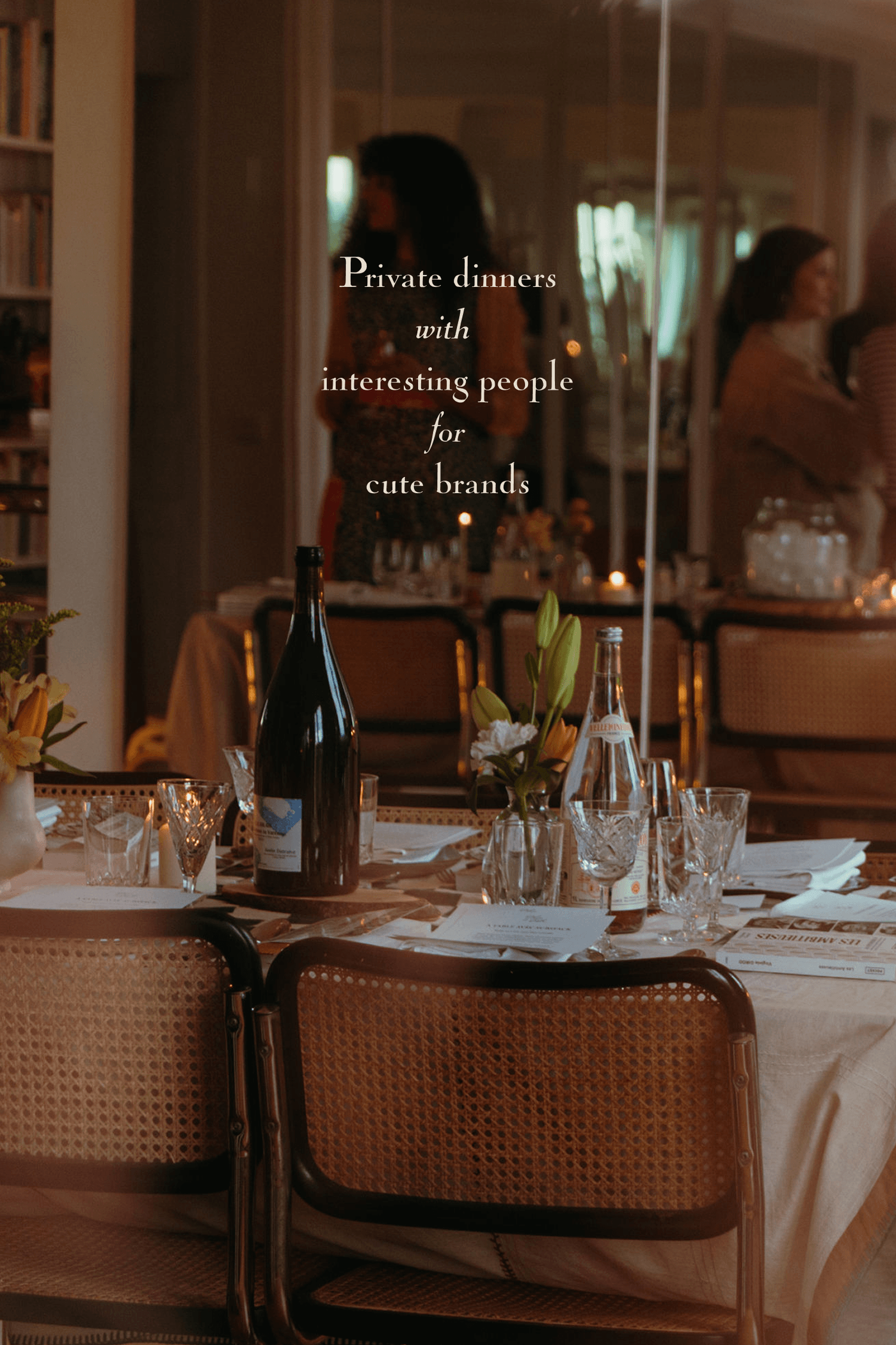 A candlelit dinner table set with wine bottles, glassware, and rattan-back chairs in a softly lit dining room, overlaid with the text "Private dinners with interesting people for cute brands."