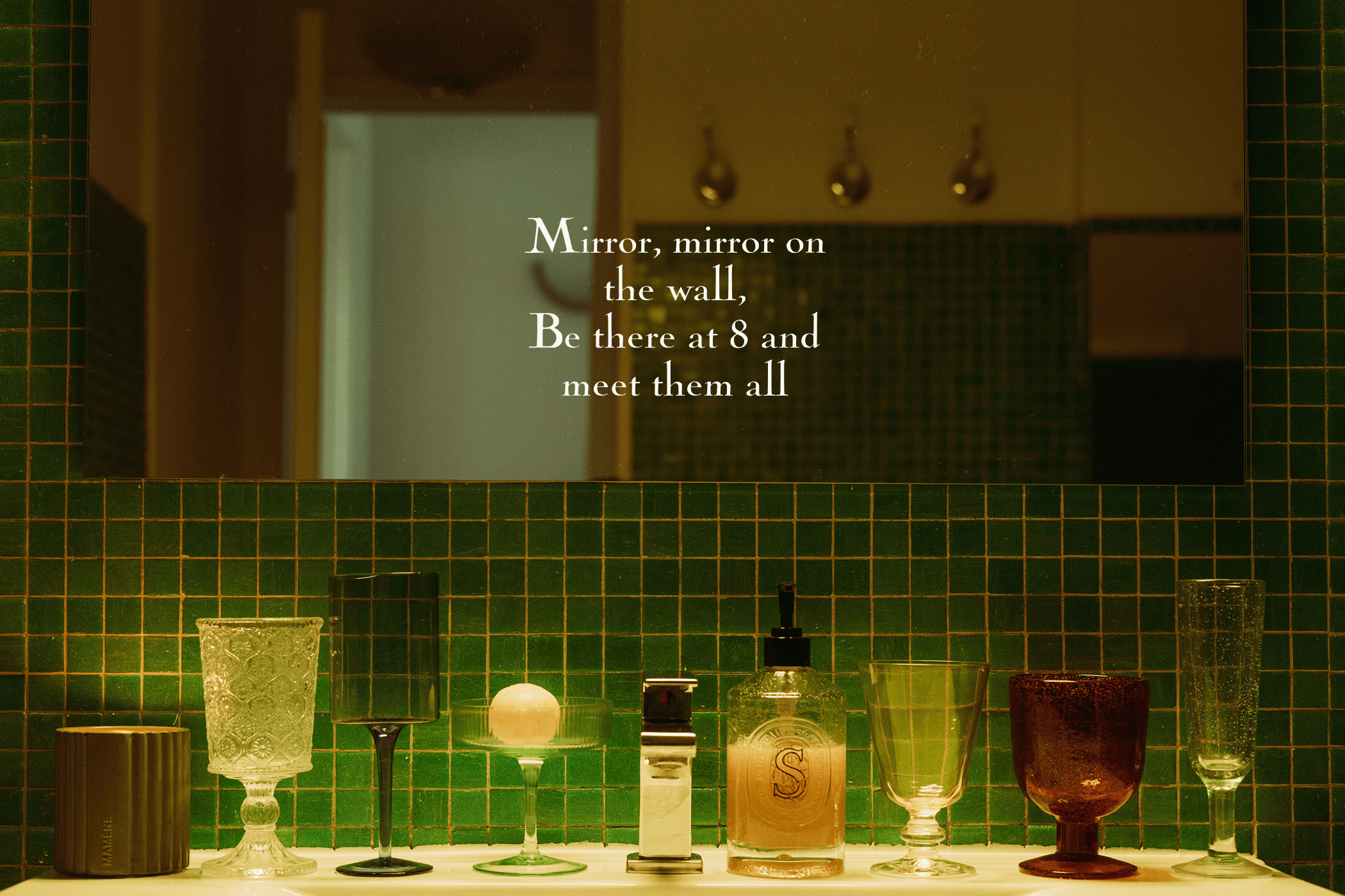 Dark green-tiled bathroom with assorted glassware and bottles, overlaid with the text "Mirror, mirror on the wall. Be there at 8 and meet them all."