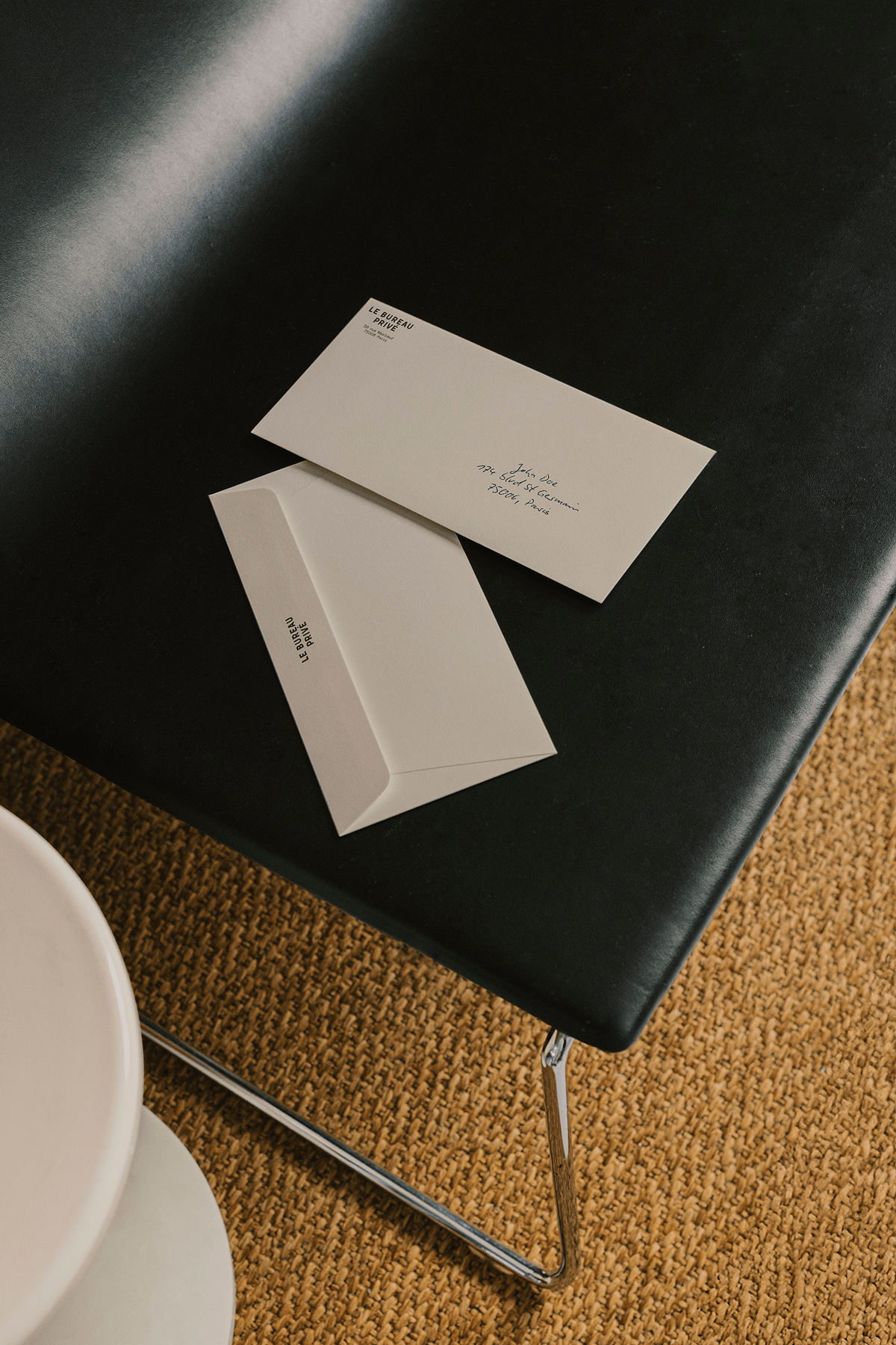Overhead shot of cream envelopes resting on a black leather chair, with a woven rug below.