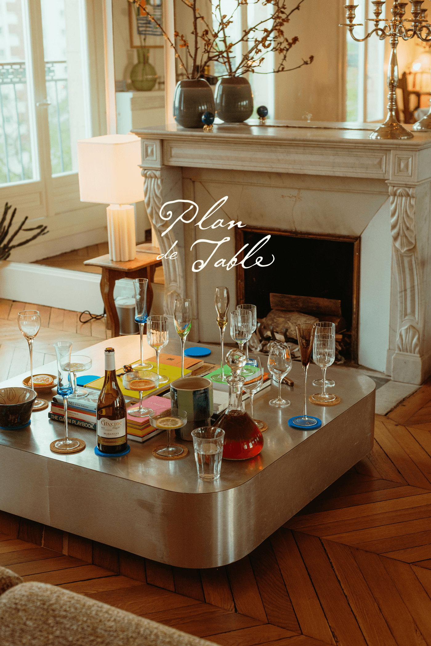 A Parisian living room coffee table styled with candles, glassware, and small dishes for an intimate dinner, overlaid with the "Plan de Table" logo.