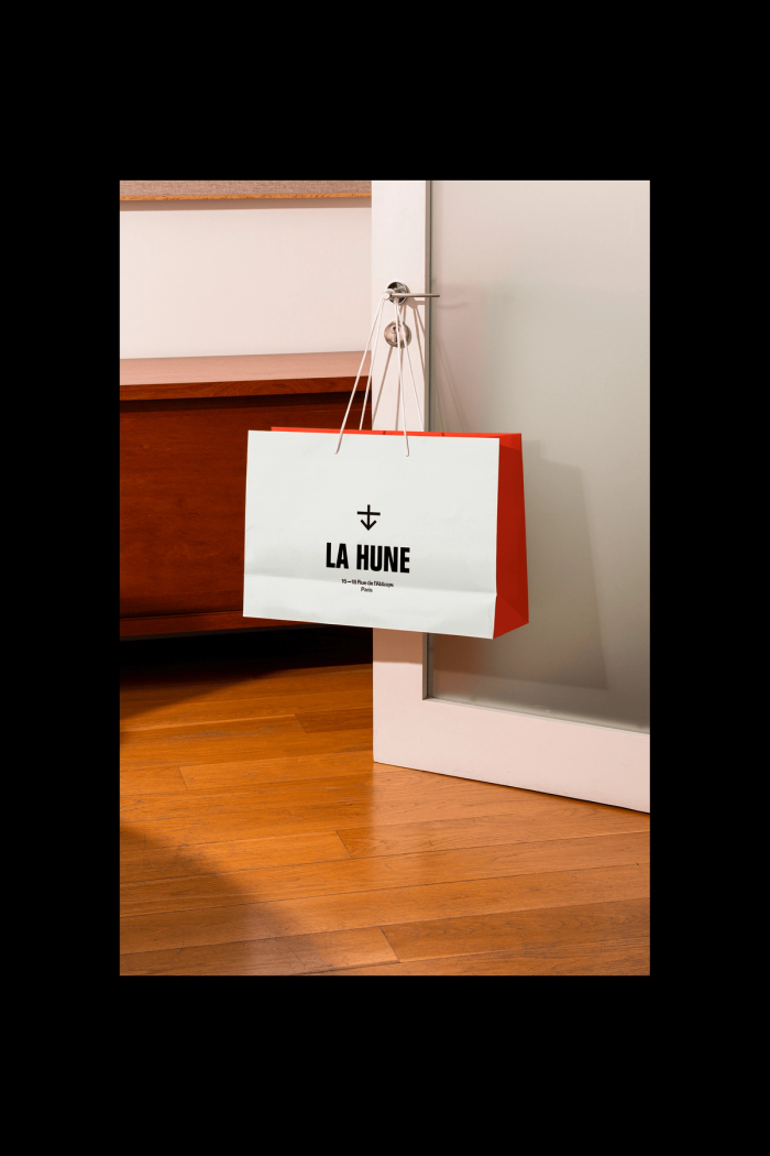 La Hune paper bag placed on the floor in a bright interior, next to a wooden cabinet.