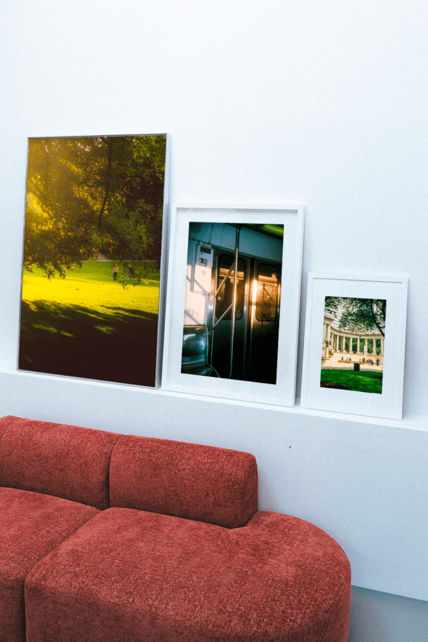 Three framed photo prints leaning against a white wall above a rust-colored sofa.
