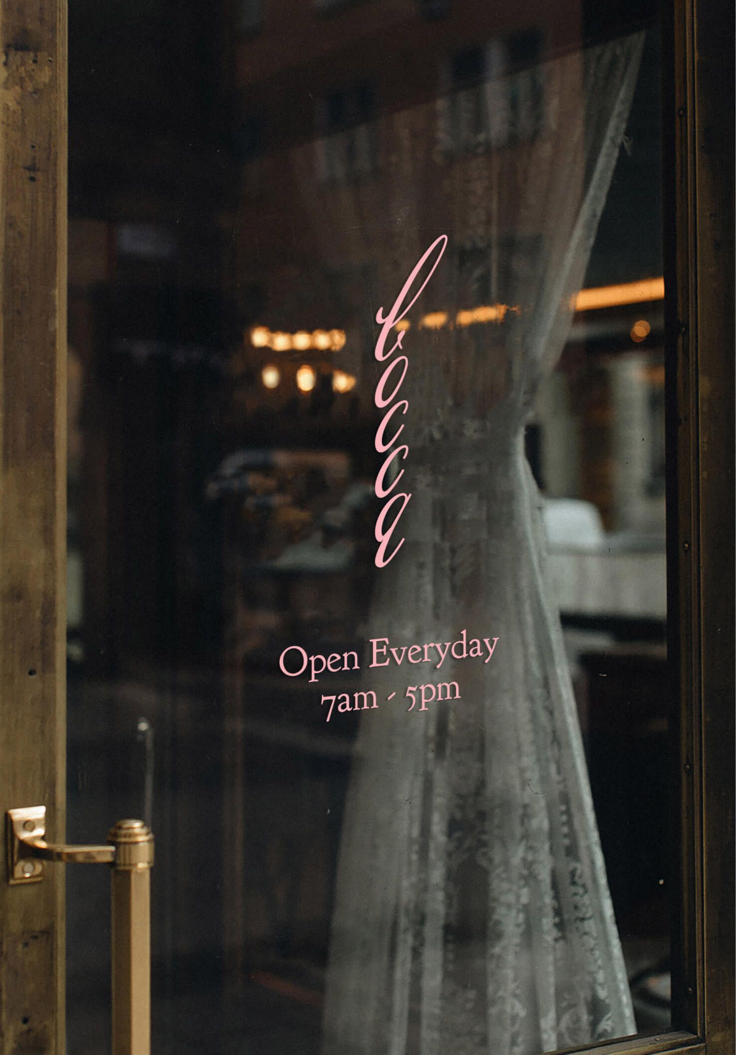 Close-up of the café's glass door at night, showing the pink cursive "Bocca" logo and "Open Everyday 7am - 5pm" text etched on the window, with warm interior lighting visible through sheer curtains.