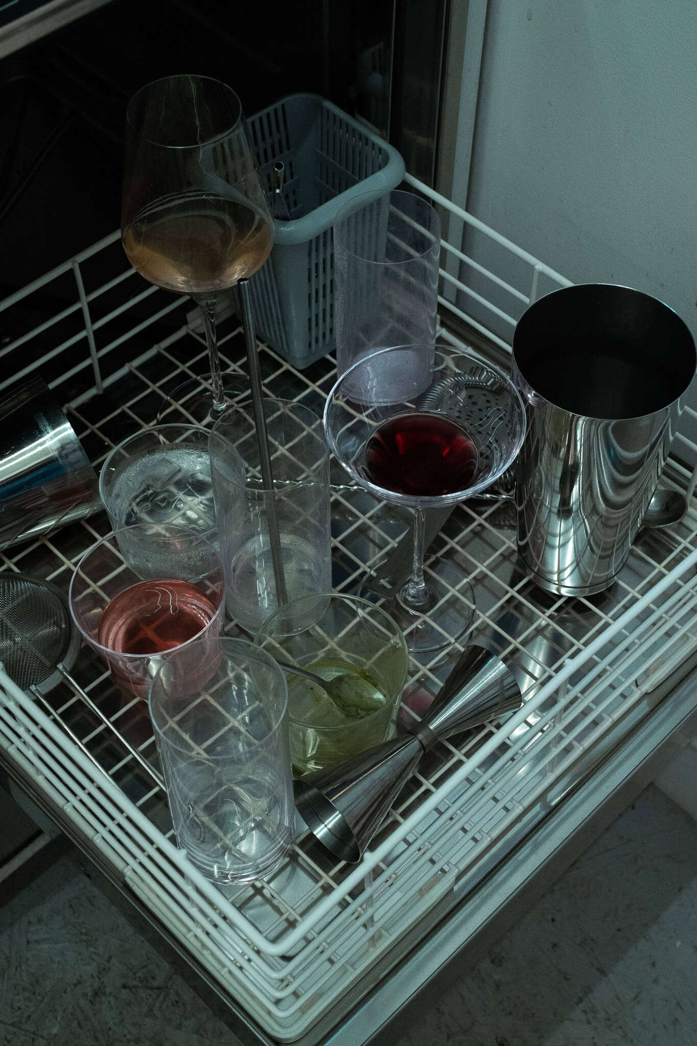 Overhead view of another bar dish washer with wine, red and green liquids in glasses, and a metal jigger.