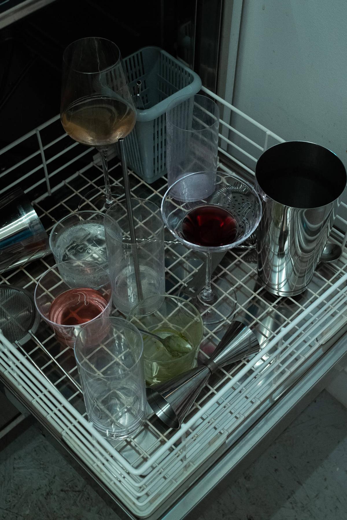 Overhead view of another bar dish washer with wine, red and green liquids in glasses, and a metal jigger.