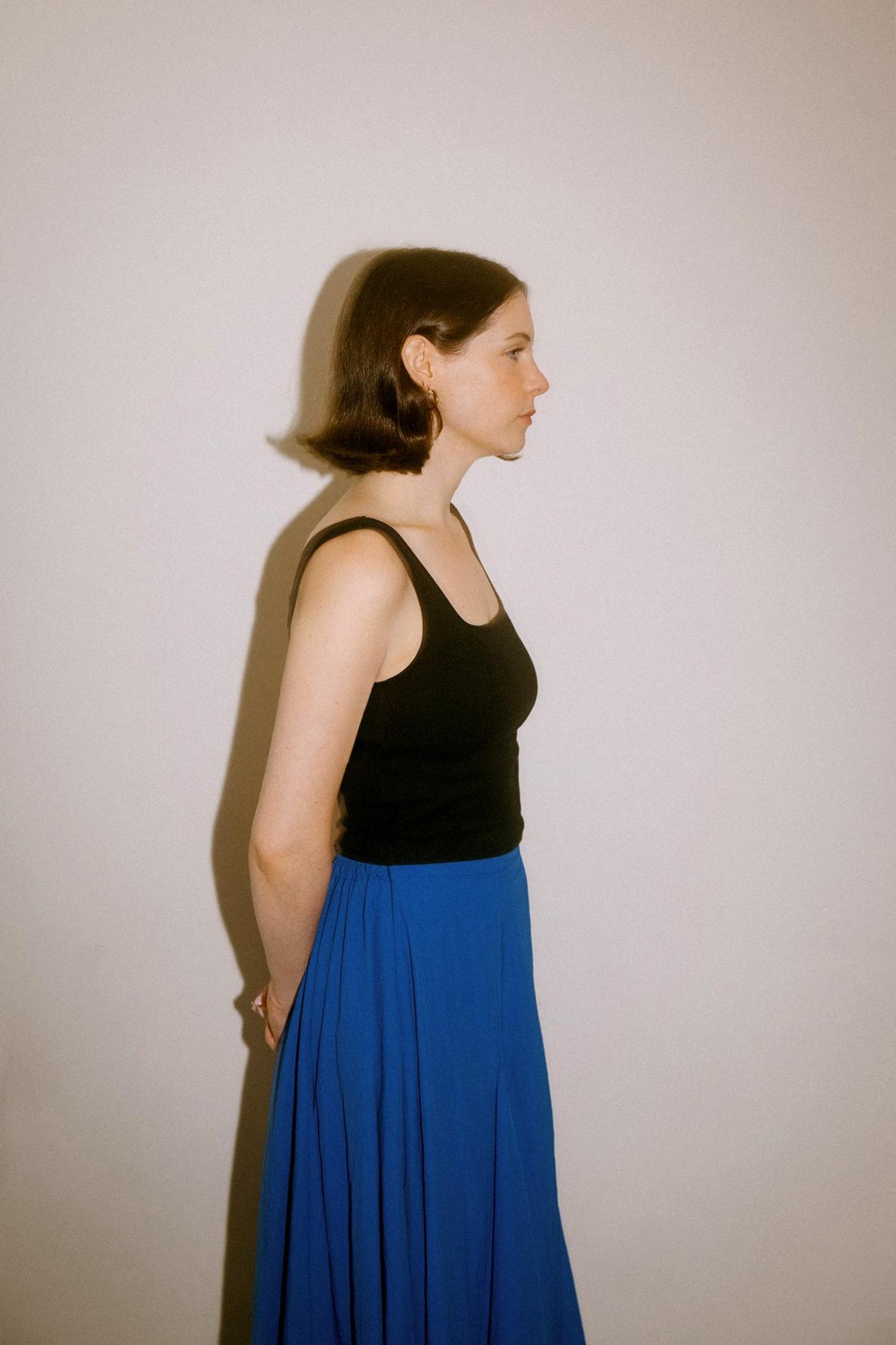 Standing profile flash photo of French Bread Studio founder, Sarah Bourge, wearing a blue skirt.