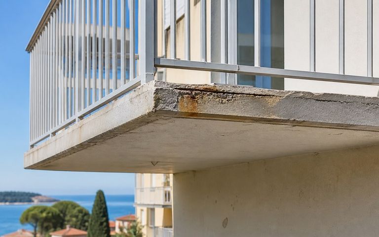 Nez de balcon en béton fissuré avec traces de corrosion face à la mer