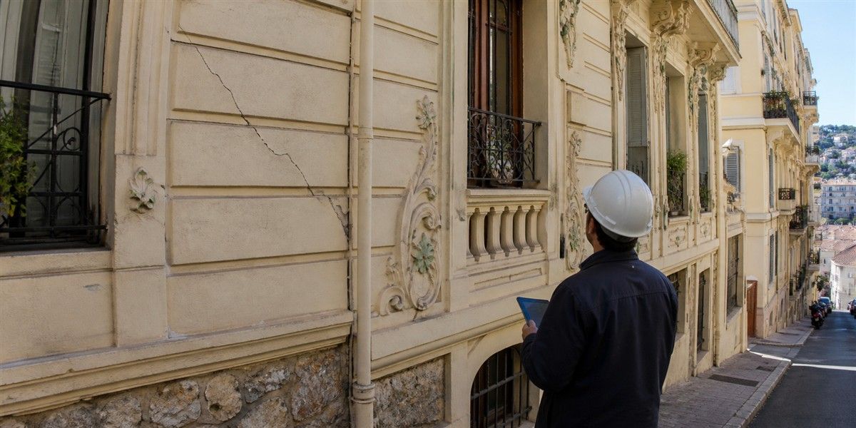 Expert inspectant une fissure sur la façade Art nouveau d’un immeuble ancien dans une rue en pente évoquant Beausoleil