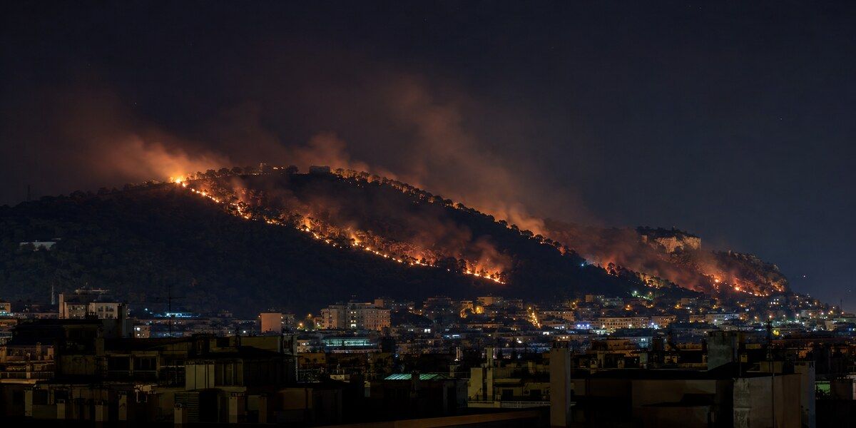 Ligne de feu nocturne progressant sur une colline boisée dominant les quartiers éclairés de Nice